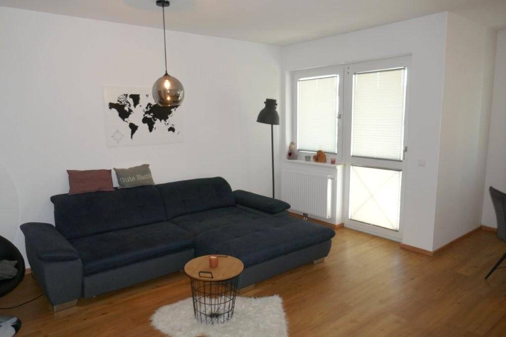 Gemütliches Wohnzimmer mit dunklem Ecksofa, Holzboden und großem Fenster für viel Tageslicht.