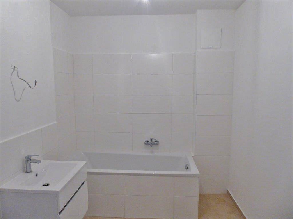 Helles Badezimmer mit weißen Fliesen, Badewanne und modernem Waschtisch.