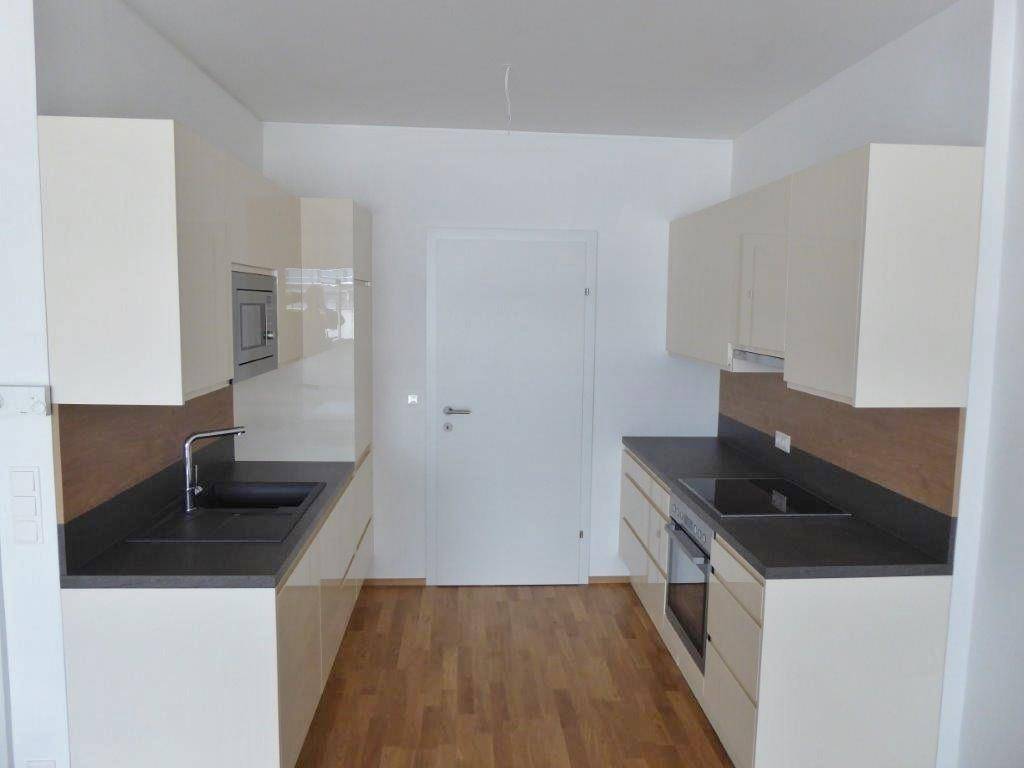 Moderne Küche mit hellen Schränken, dunkler Arbeitsplatte und Holzboden.