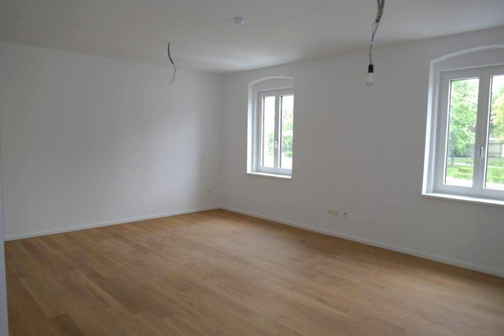 Großer, heller Wohnraum mit zwei Fenstern, Holzboden und viel Tageslicht.
