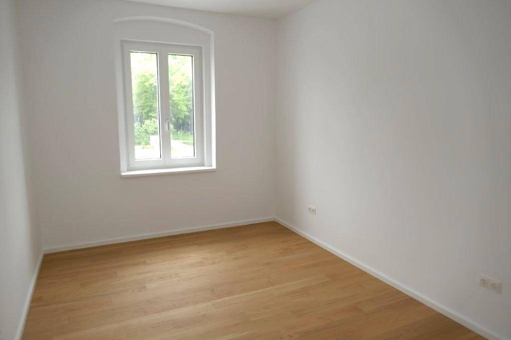 Helles Schlafzimmer mit einem Fenster, Holzboden und Blick ins Grüne.