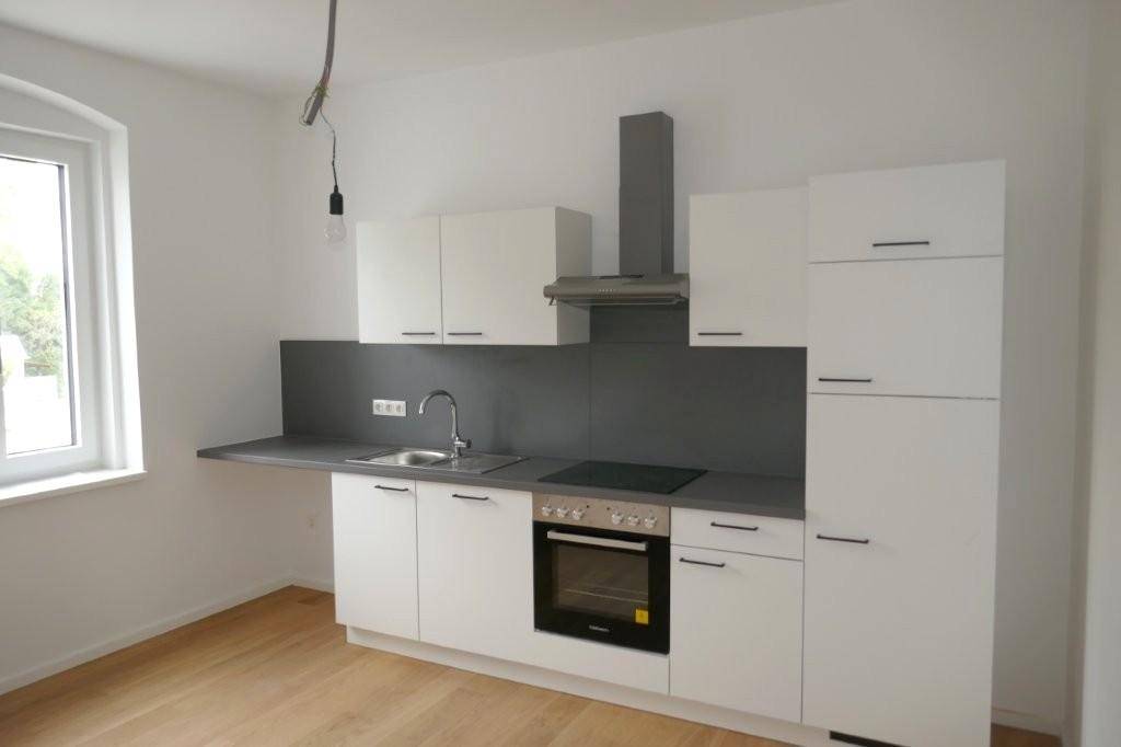 Moderne Einbauküche in Weiß und Grau mit Kochfeld, Backofen und Dunstabzugshaube.