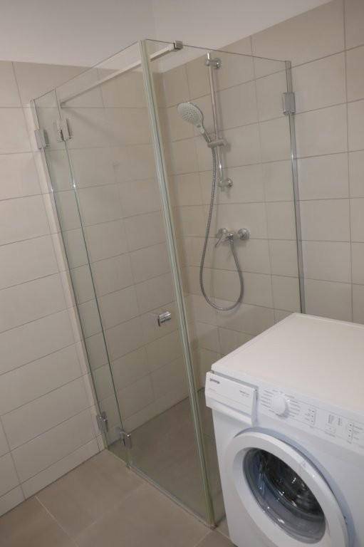 Modernes Badezimmer mit Glasdusche und Waschmaschine, hell gefliest.