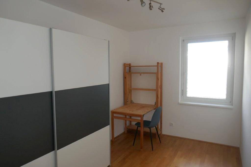 Zimmer mit Schiebetürenschrank, kleinem Schreibtisch und Fenster.