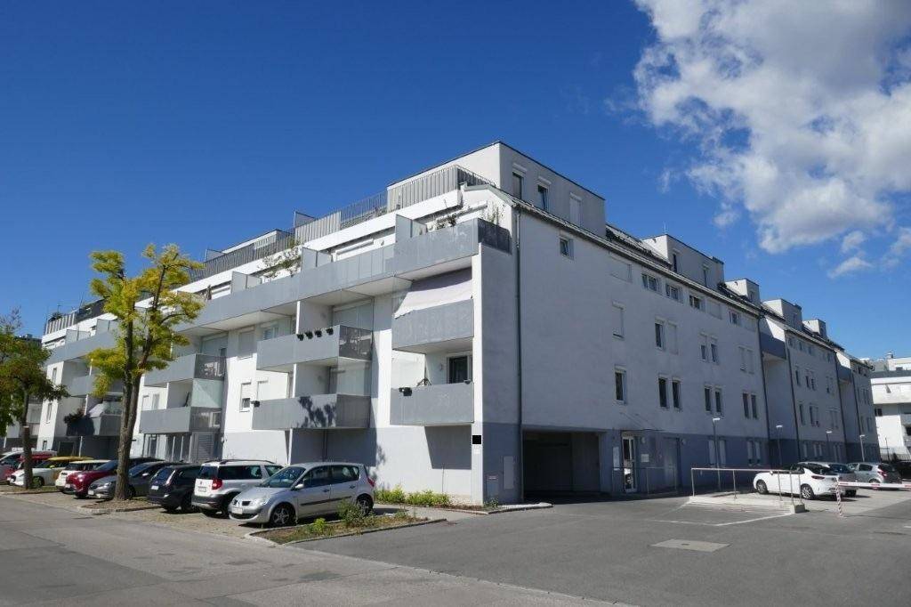 Modernes Mehrfamilienhaus mit Balkonen und Außenparkplätzen unter blauem Himmel.