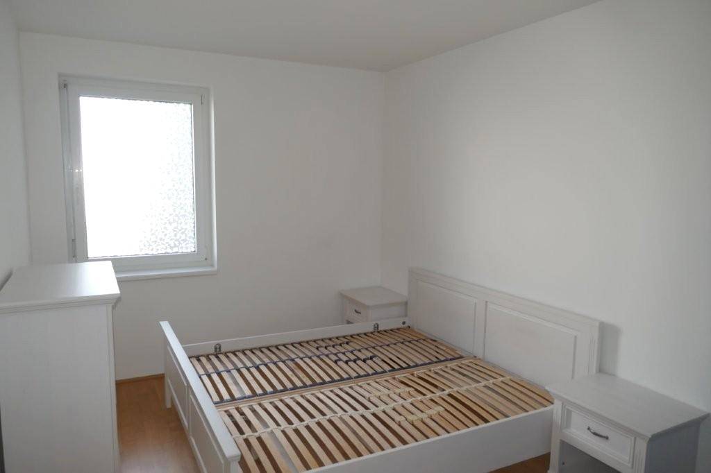 Helles Schlafzimmer mit weißem Bettrahmen, Kommode und Fenster.