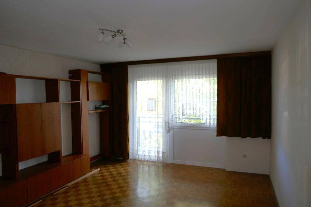 Helles Wohnzimmer mit Parkettboden, Holzschrankwand und Zugang zum Balkon.