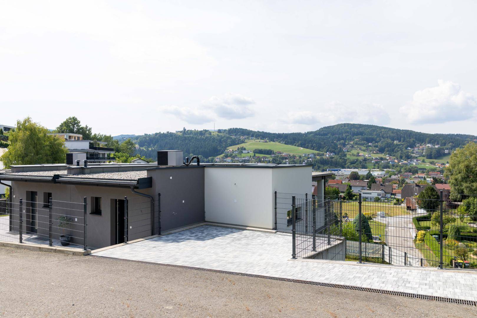 Außenansicht eines modernen Gebäudes mit gepflastertem Vorplatz und weitem Blick über die Landschaft.