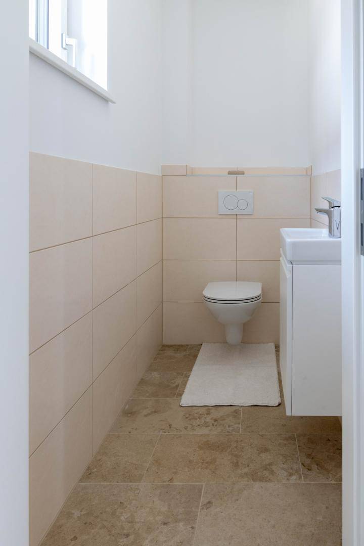 Modernes Gäste-WC mit beigefarbenen Fliesen, wandhängendem WC und kleinem Waschbecken.