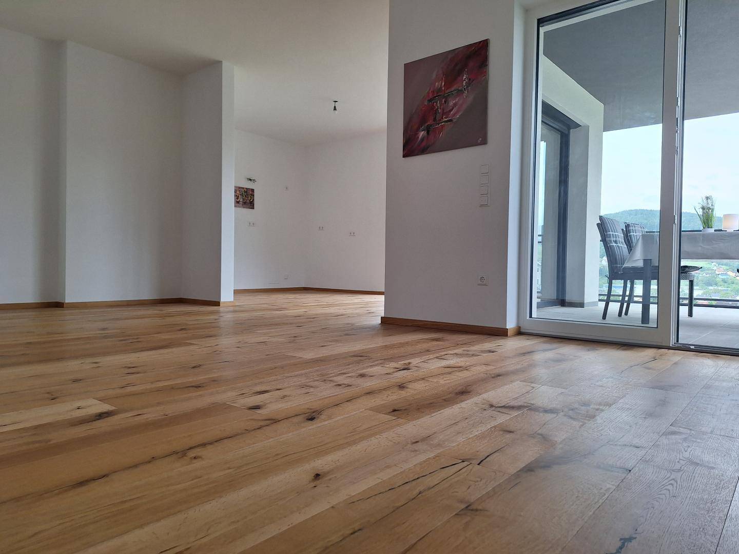 Geräumiger Wohnbereich mit Holzboden und Zugang zu einem Balkon mit schöner Aussicht.