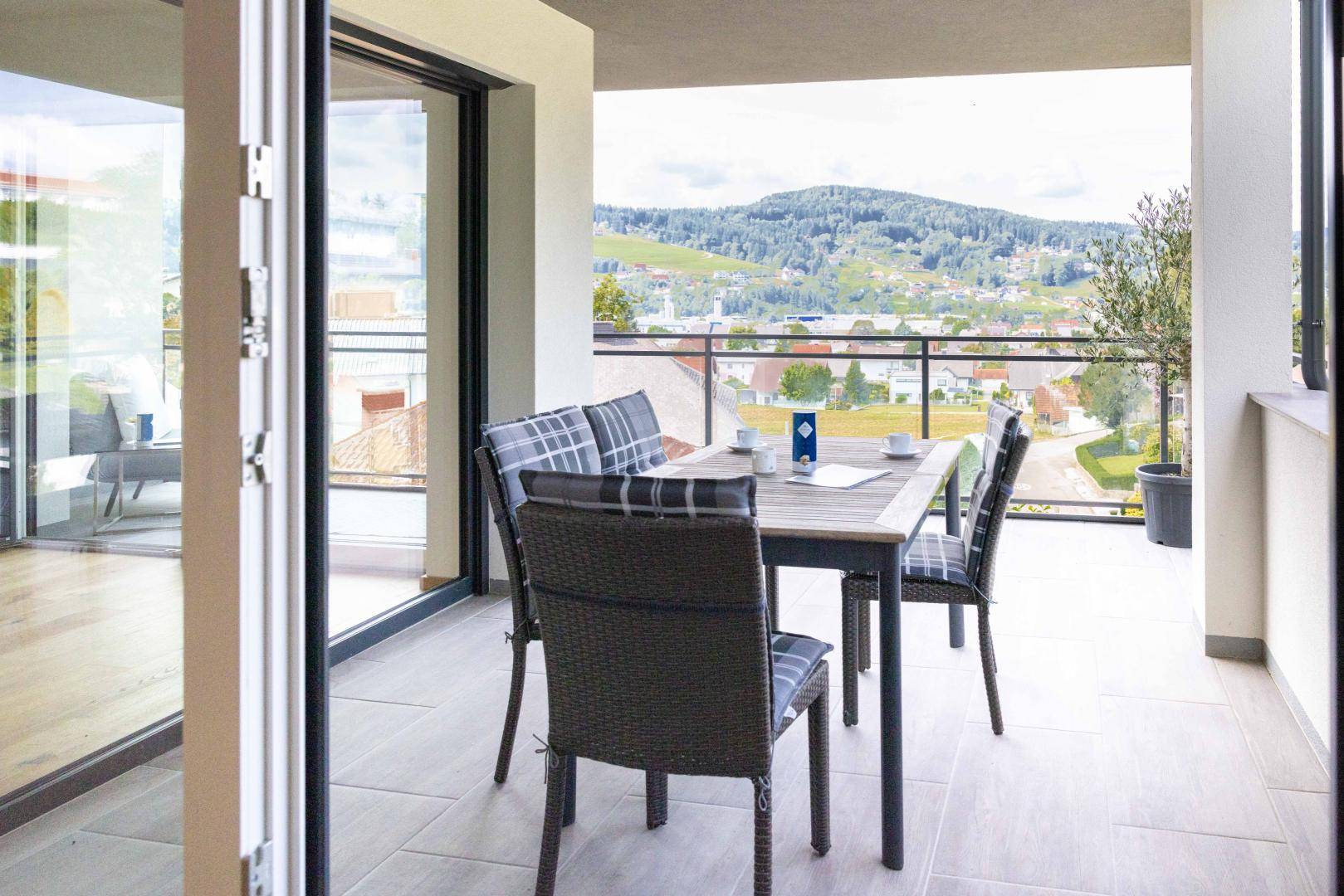 Möblierter Balkon mit Esstisch und Stühlen, bietet einen schönen Blick ins Grüne.