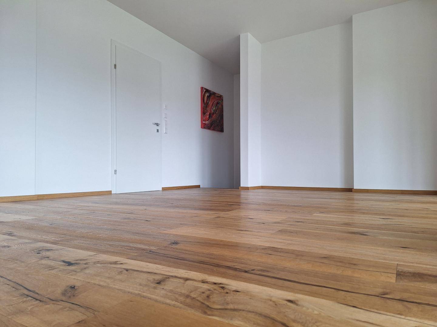 Heller Innenraum mit neuem Holzboden und weißen Wänden, bereit für die Einrichtung.