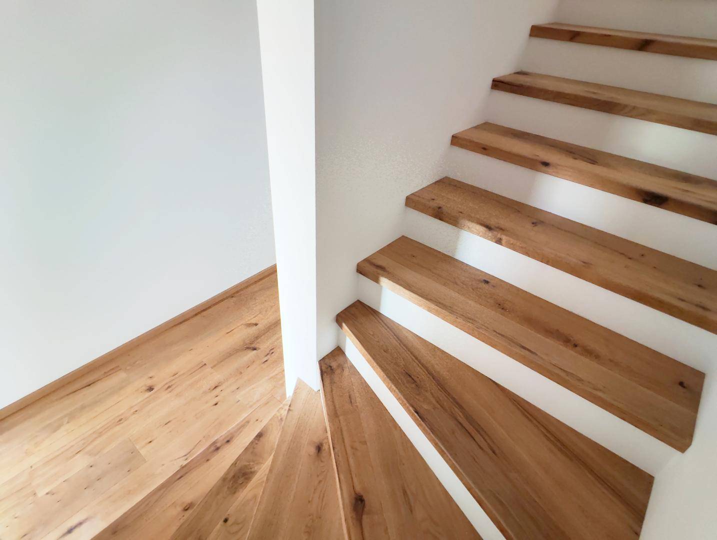 Moderne Holztreppe mit offenen Stufen und hellem Holzboden im Eingangsbereich.