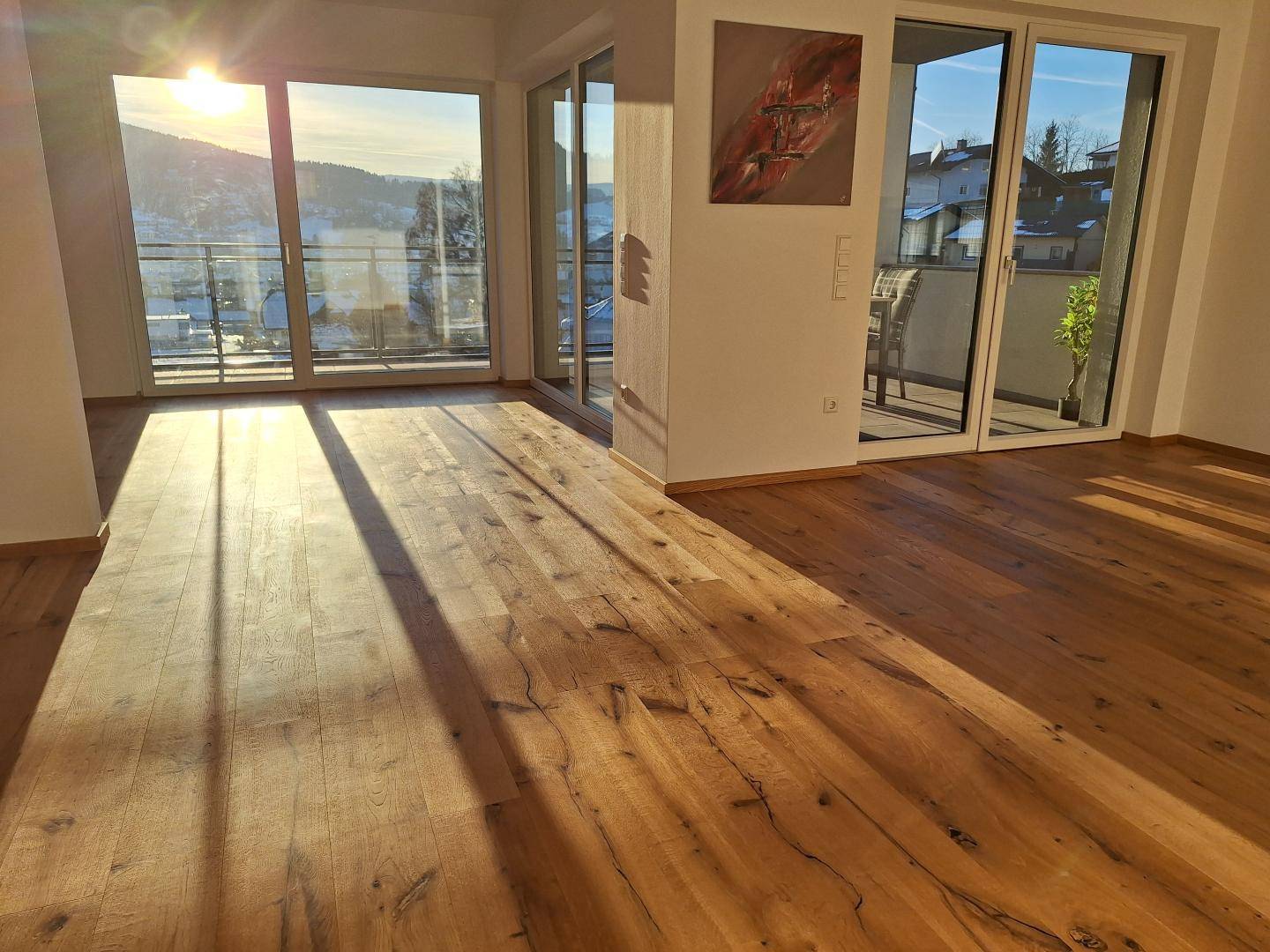 Sonnenverwöhnter Wohnbereich mit Holzboden und großen Fenstern, die viel Licht hereinlassen.
