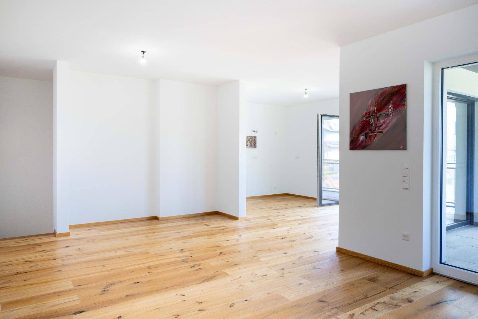Heller Wohnraum mit Holzboden und Zugang zu einem Balkon, bereit für die individuelle Gestaltung.