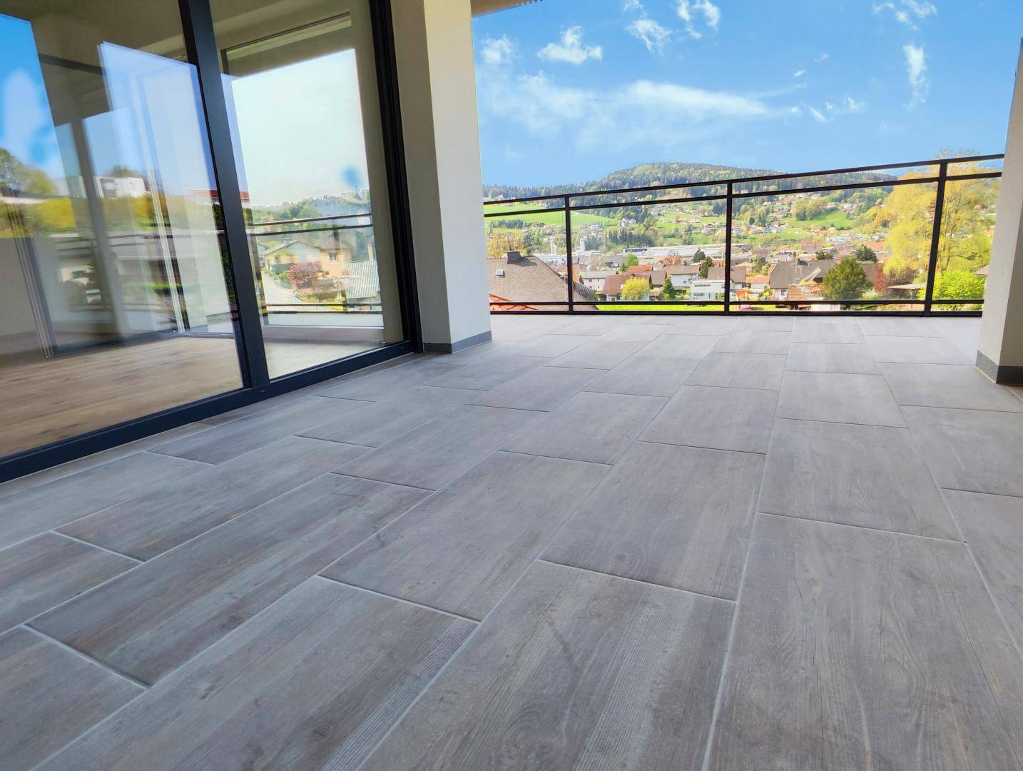 Großer Balkon mit Fliesenboden und Glasgeländer bietet einen weiten Blick über die Landschaft.