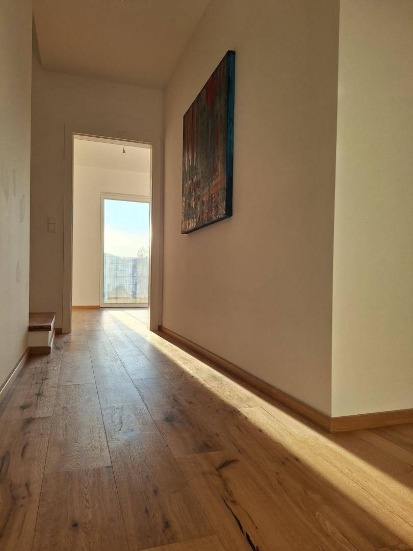 Heller Flur mit Holzboden und einem Kunstwerk, durchflutet von natürlichem Sonnenlicht.