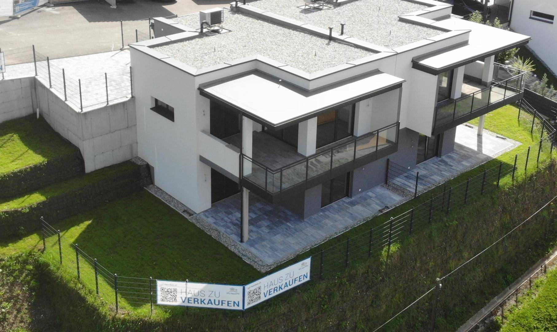 Moderne Doppelhaushälfte mit Flachdach und gepflegtem Rasen in Hanglage.