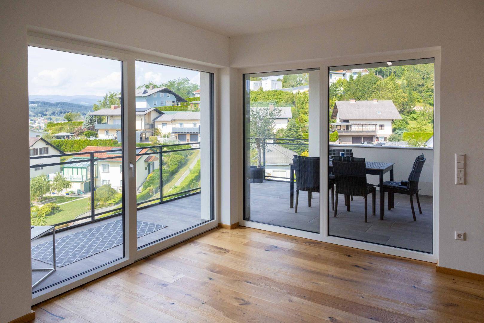Heller Innenraum mit großen Fenstern und Zugang zu einem Balkon mit Essbereich und schöner Aussicht.