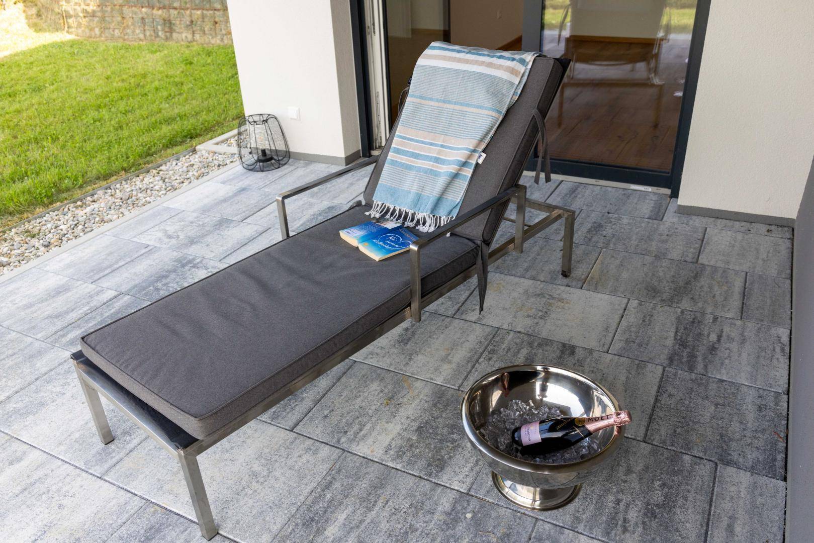 Detailaufnahme eines Liegestuhls und Sektkühlers auf der gefliesten Terrasse, bereit für entspannte Momente.