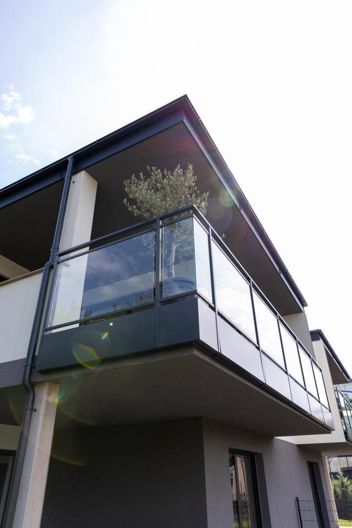 Moderne Architektur des Gebäudes mit mehreren Balkonen und eleganten Glasgeländern unter blauem Himmel.