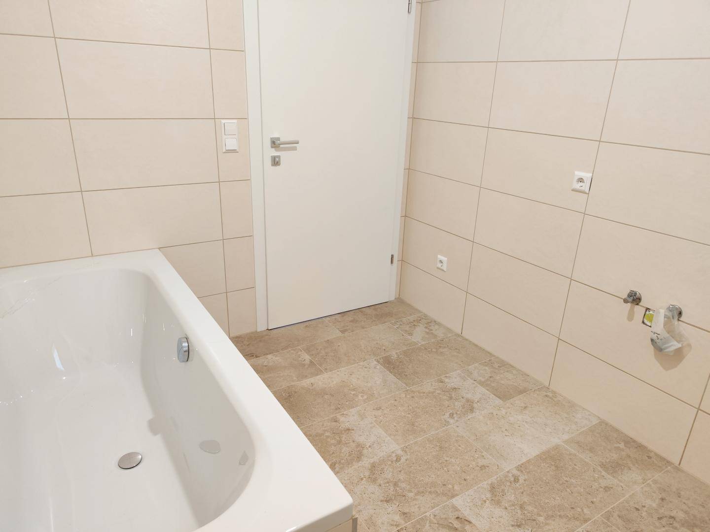 Badezimmer mit beigefarbenen Fliesen an Wänden und Boden, sowie einer Badewanne.