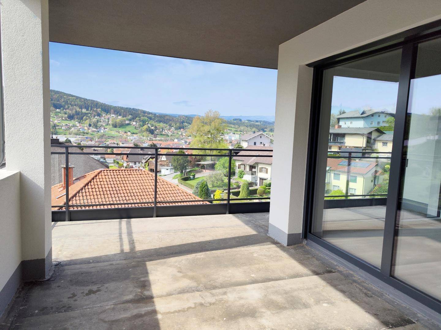 Geräumiger Balkon mit Glasgeländer und Panoramablick über die Dächer und grüne Landschaft.