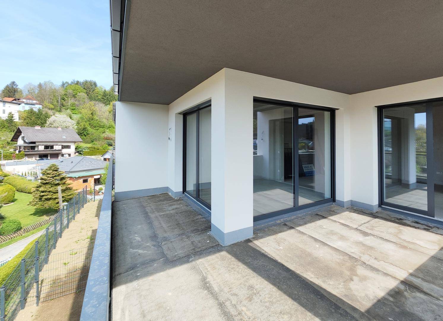 Breiter Balkon mit Schiebetüren und weitem Blick auf die umliegende Hügellandschaft und Häuser.