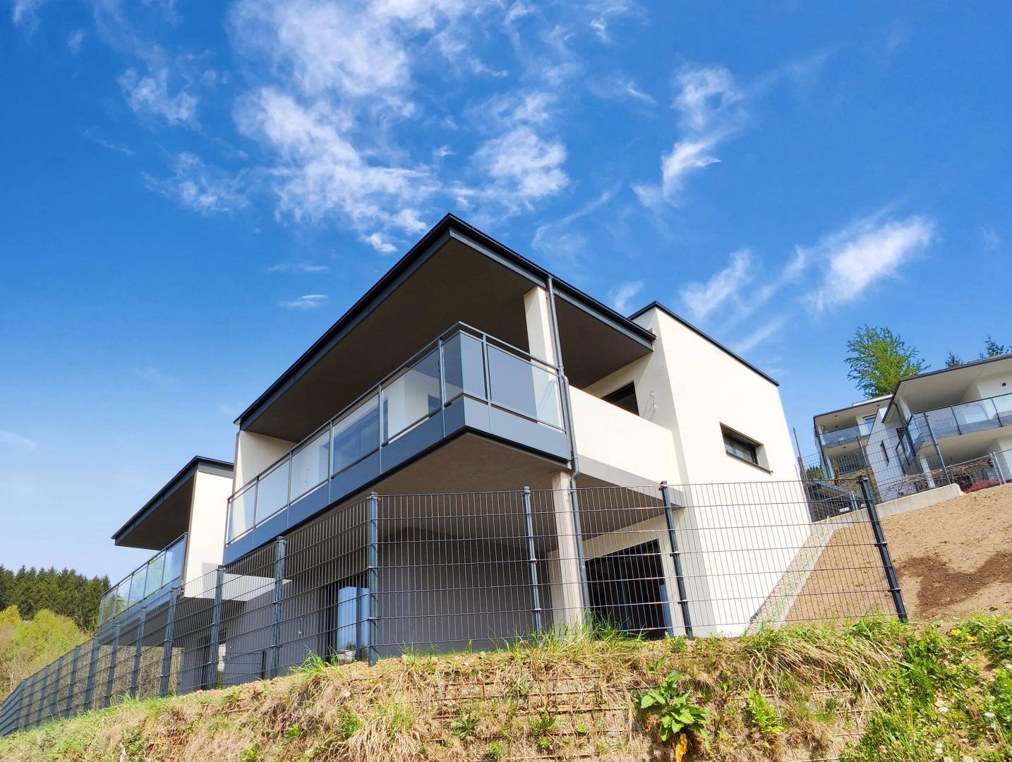 Ansicht der modernen Gebäudefassade mit großen Balkonen und Glasgeländern unter blauem Himmel.