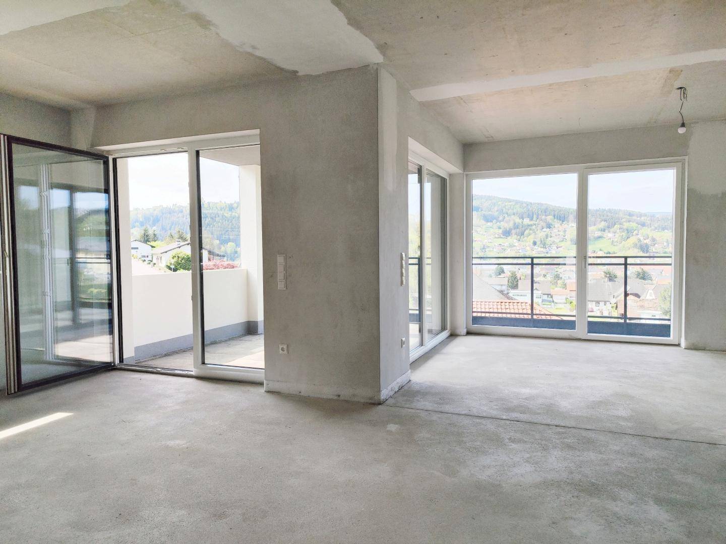 Unfertiger Wohnbereich mit großen Fensterfronten, Balkonzugang und weitem Blick ins Grüne.