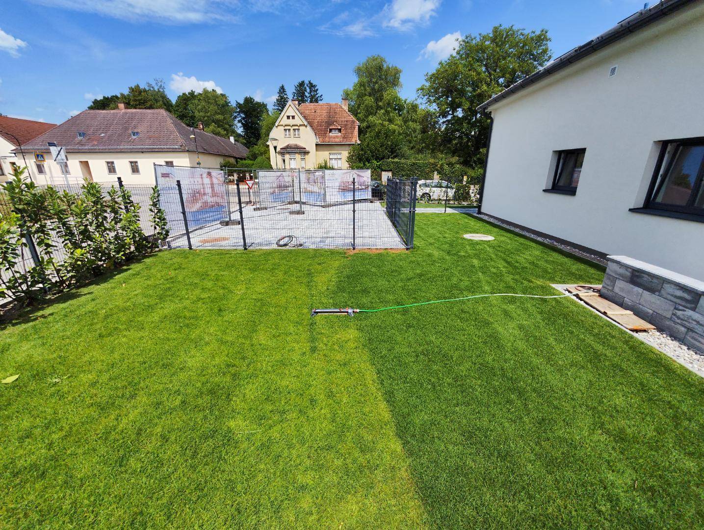 Großer, gepflegter Rasenbereich mit Bewässerungssystem und Blick auf die Nachbarschaft.