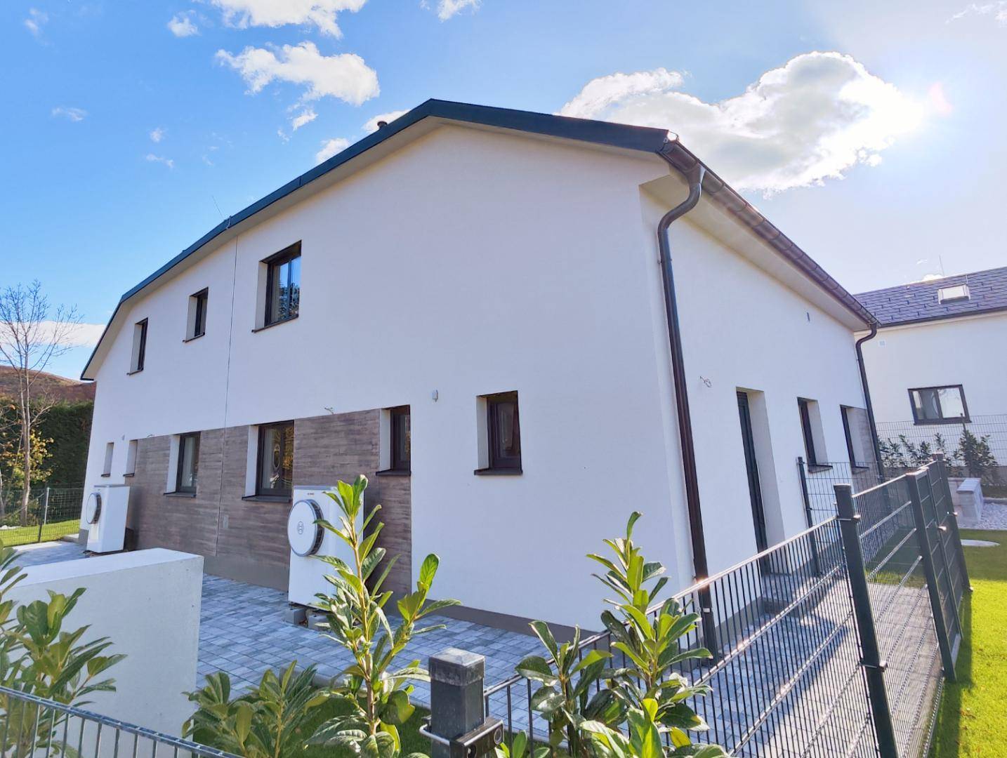 Rückansicht des modernen Hauses mit heller Fassade und Wärmepumpe im Außenbereich.