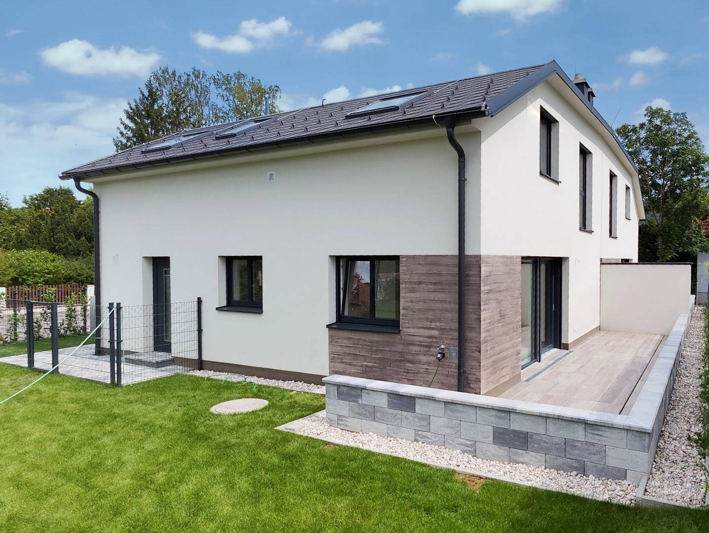 Seitenansicht des Hauses mit gepflasterter Terrasse, kleiner Rasenfläche und moderner Fassade.