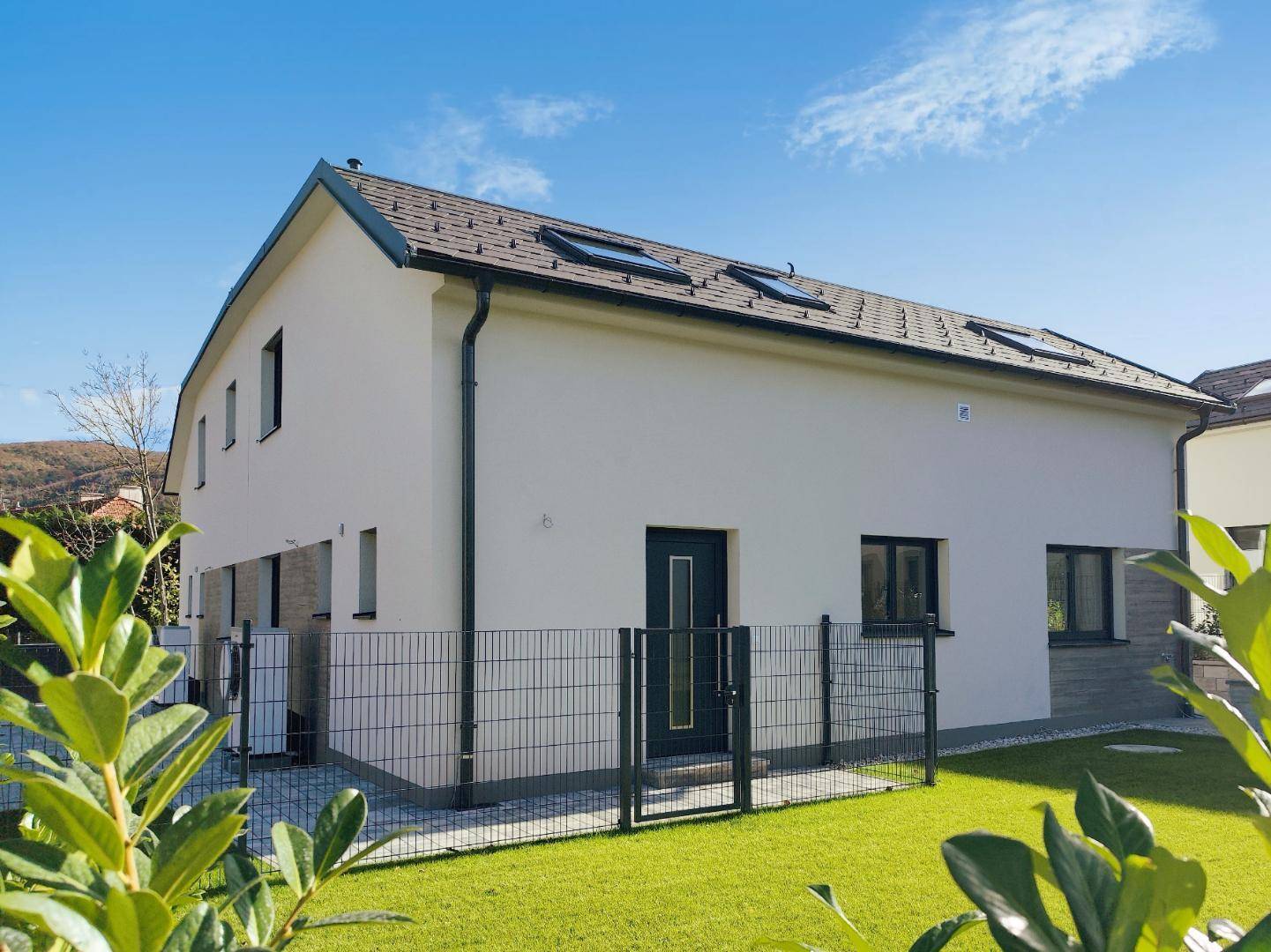 Vorderansicht des modernen Hauses mit Eingangstür, Zaun und gepflegtem Vorgarten.