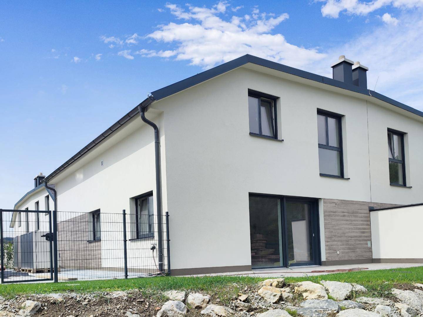 Seitenansicht einer modernen Doppelhaushälfte mit weißer Fassade und dunklem Dach.