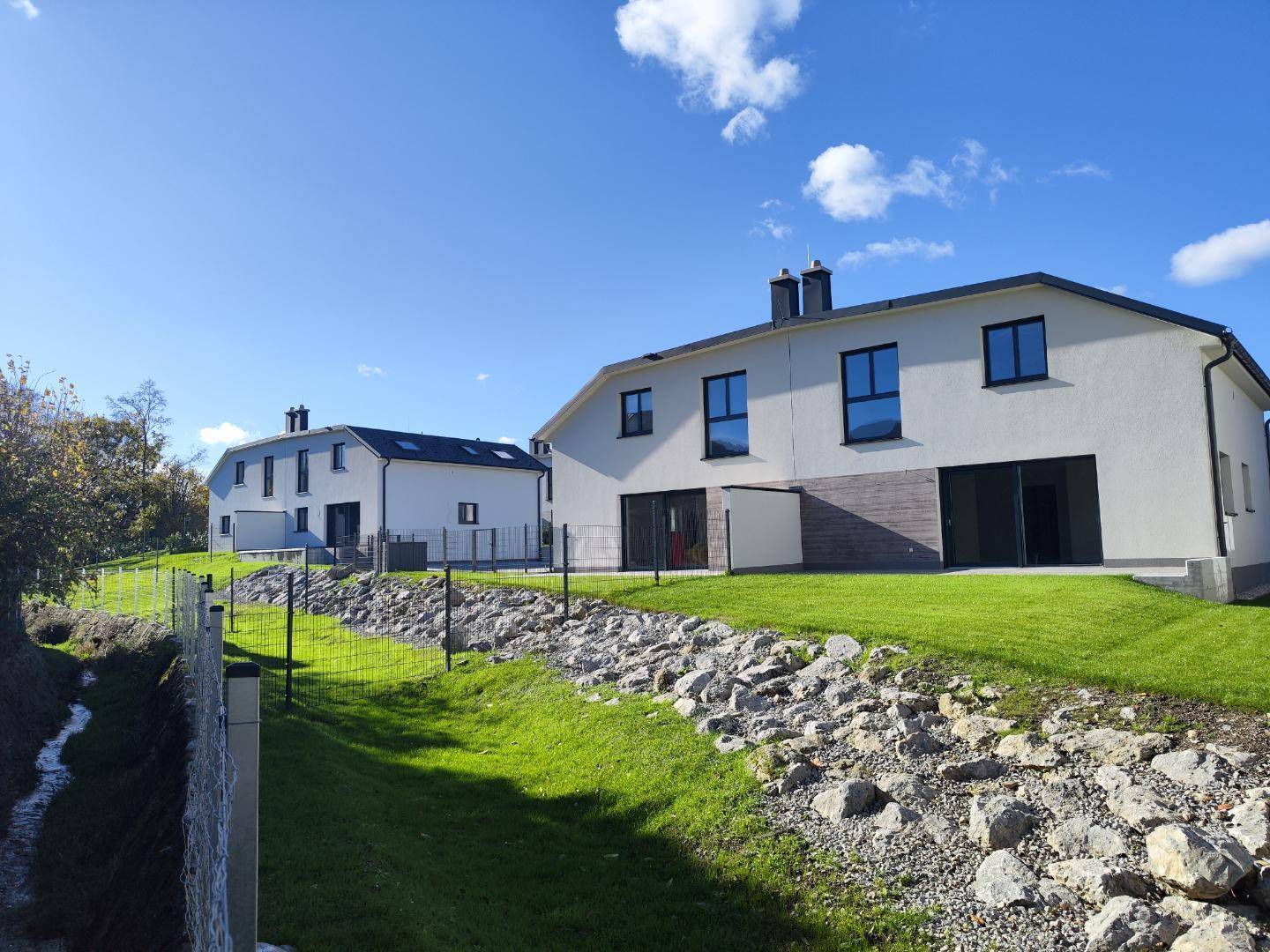 Mehrere moderne Reihenhäuser mit weißer Fassade, umgeben von Rasen und Felsen.