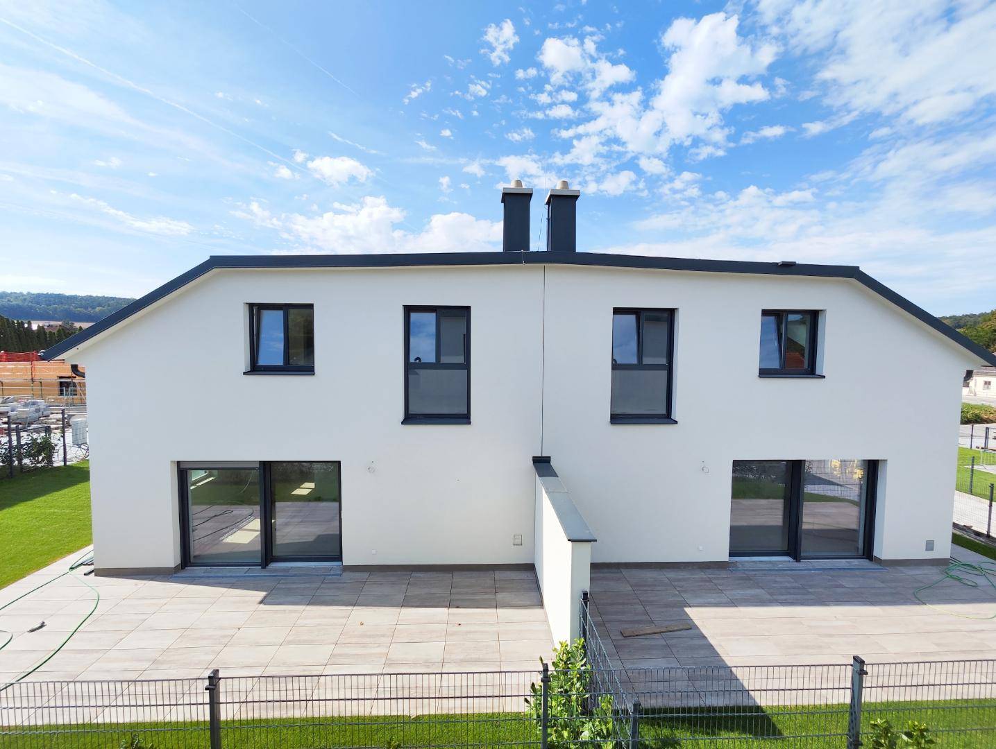 Vogelperspektive auf zwei moderne Doppelhaushälften mit großzügigen Terrassen und gepflegten Rasenflächen.