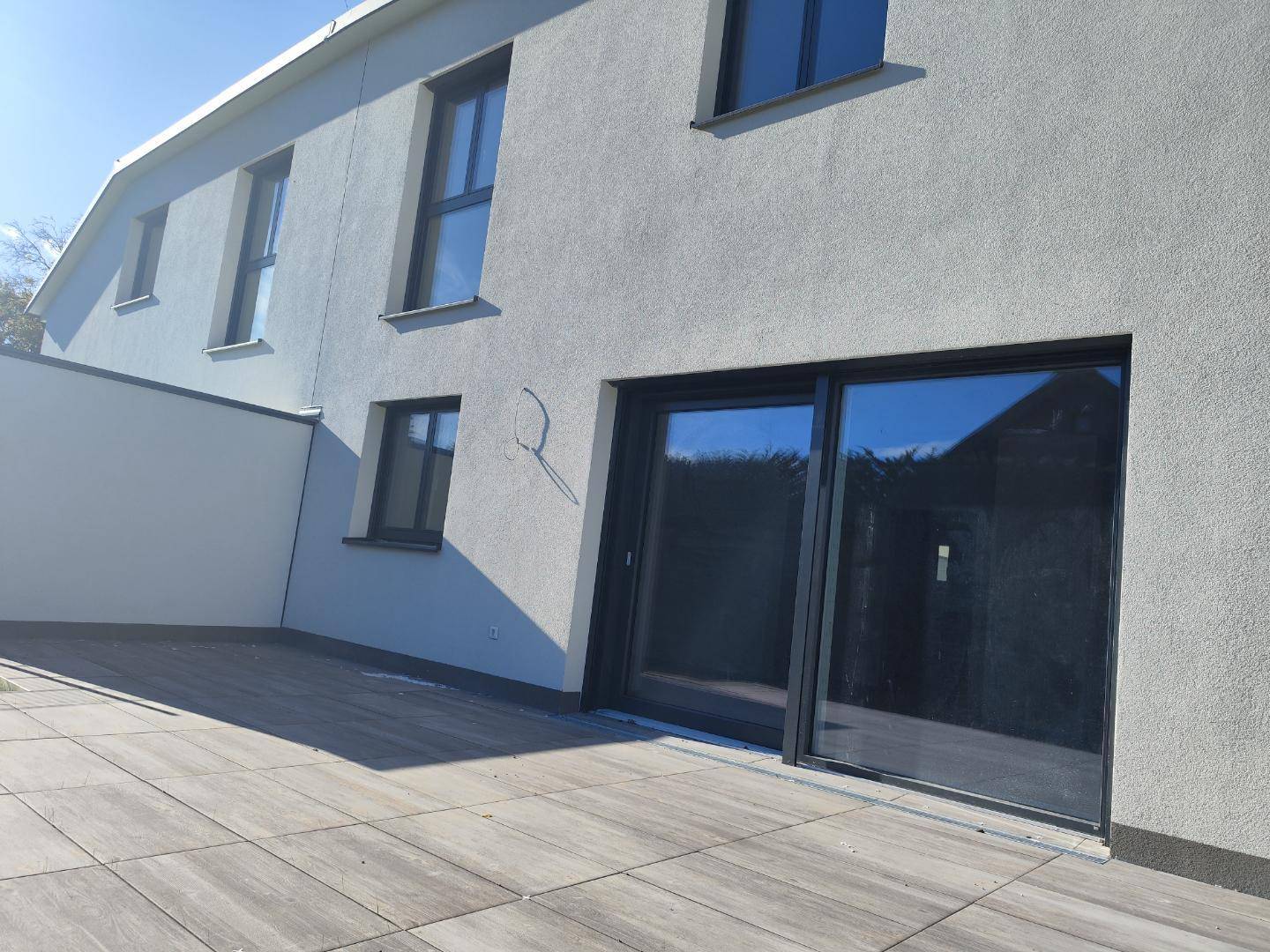 Nahaufnahme der modernen Hausfassade mit großen Schiebetüren und gepflasterter Terrasse.