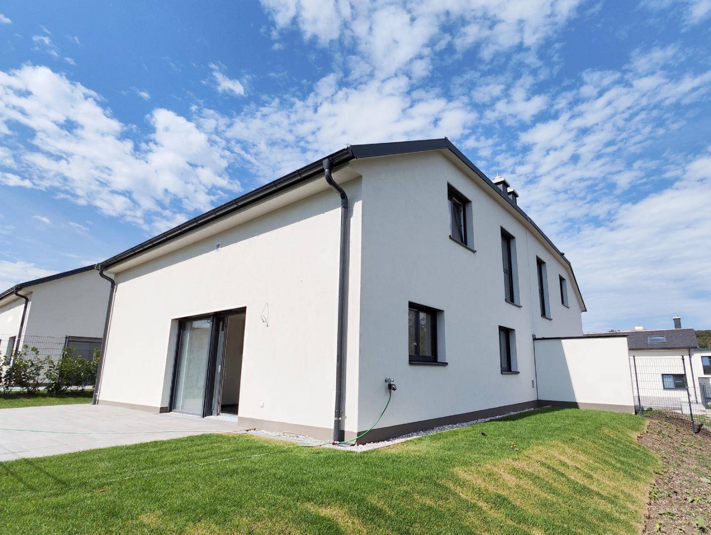 Rückseite eines modernen Hauses mit großer Schiebetür, Rasenfläche und Zugang zum Garten.