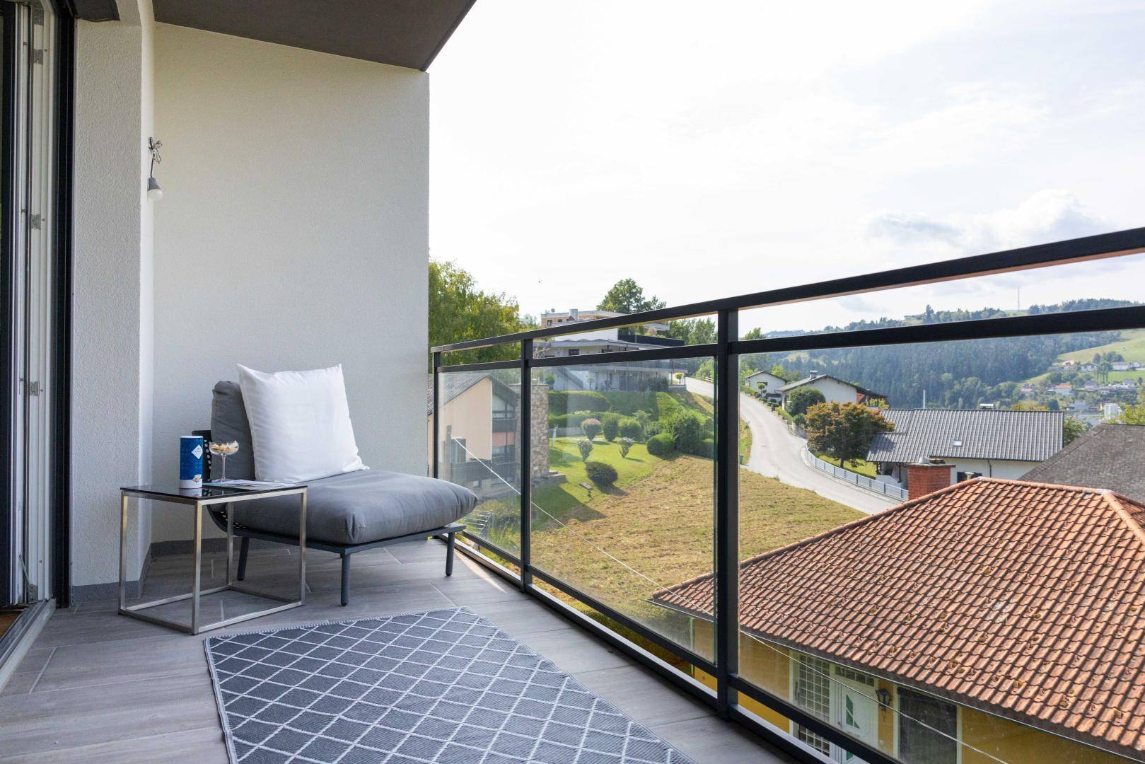 Gemütlicher Balkon mit Sitzgelegenheit und Glasgeländer, bietet einen schönen Ausblick auf die Umgebung.