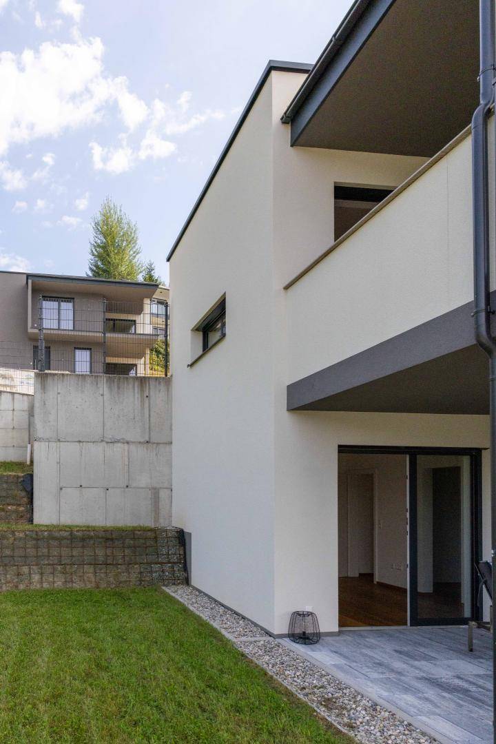 Seitenansicht eines modernen Gebäudes mit weißer Fassade und angrenzender Grünfläche.