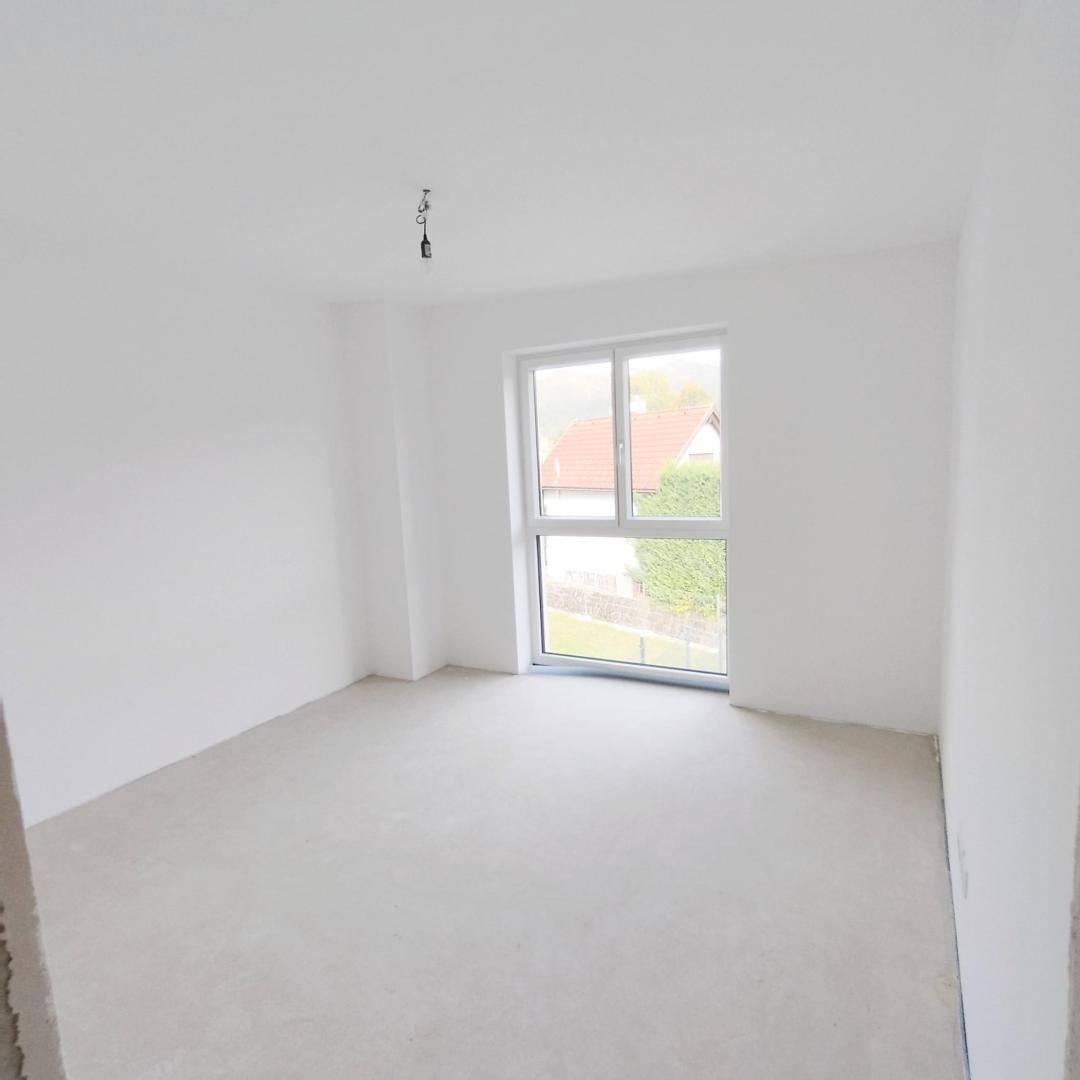 Helles, unmöbliertes Zimmer mit weiß gestrichenen Wänden und großem Fenster.