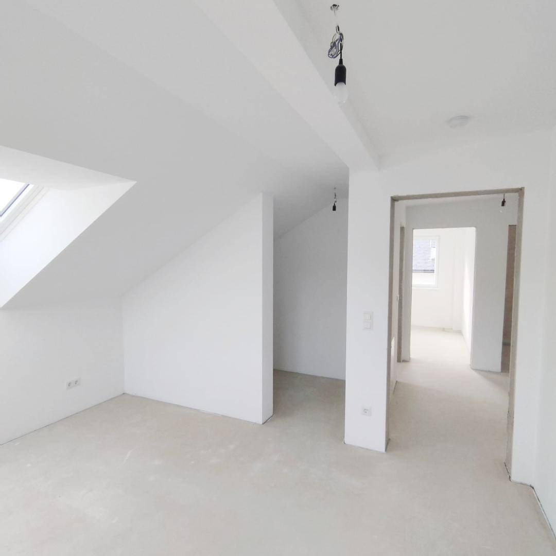 Geräumiger Dachbodenraum mit weiß gestrichenen Wänden und einem hellen Dachfenster.