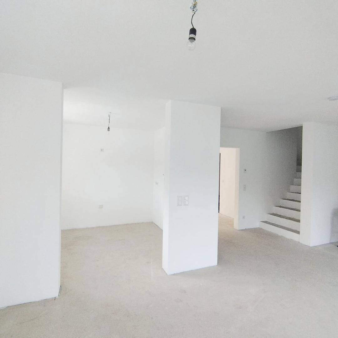 Offener Wohnbereich mit weiß gestrichenen Wänden und einer Treppe zum Obergeschoss.