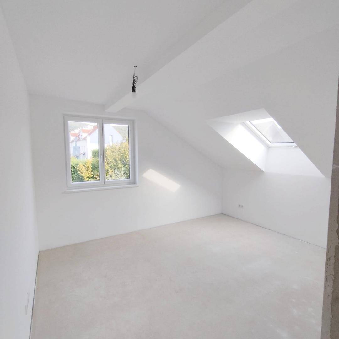 Dachzimmer mit weiß gestrichenen Wänden, Fenster und zusätzlichem Dachfenster für Helligkeit.