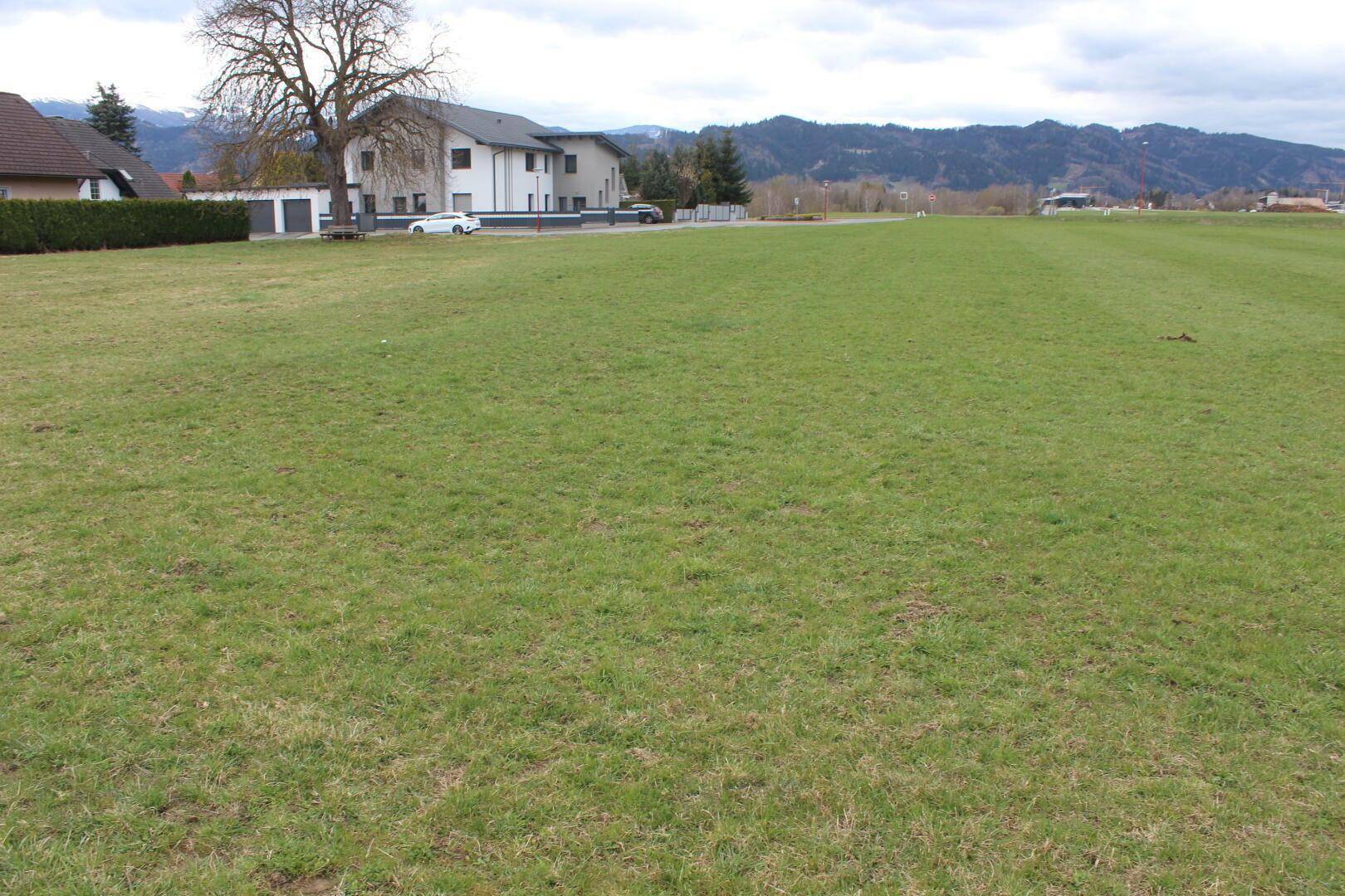 Große, offene Grünfläche mit Blick auf Wohnhäuser und die umliegende Berglandschaft.