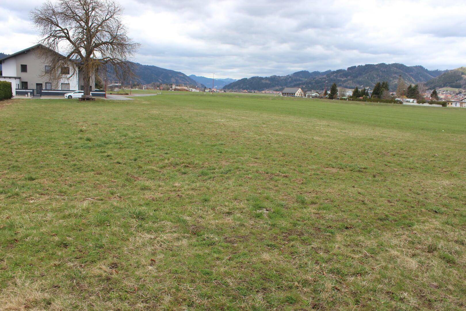 Weitläufiges Wiesengrundstück mit Fernblick auf die Berge und angrenzende Bebauung.