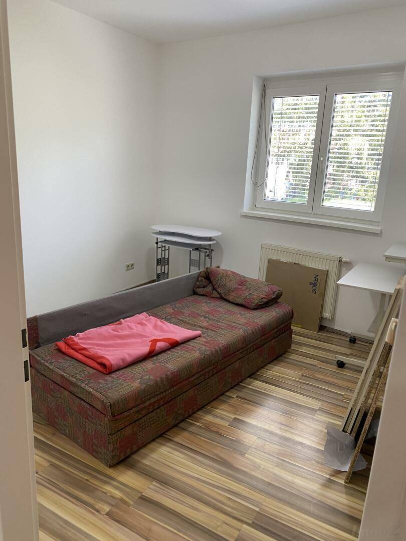Schlafzimmer mit Einzelbett, Schreibtisch und Fenster mit Jalousien, hell und gemütlich.