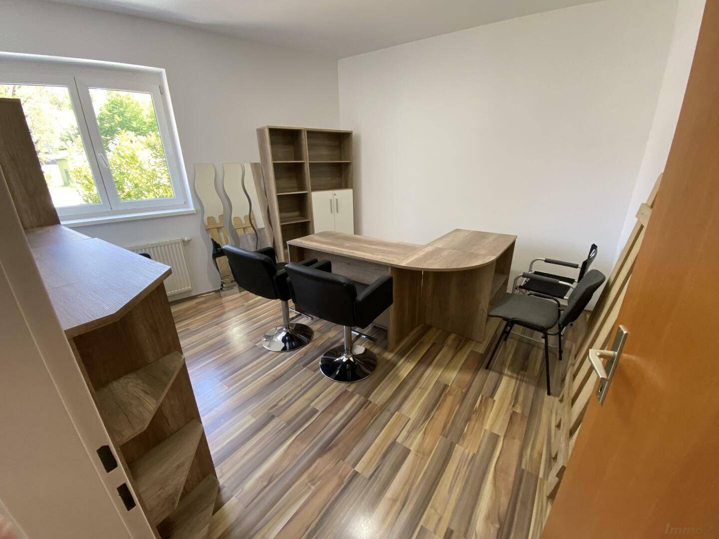 Heller Büroraum mit Laminatboden, Schreibtisch, Stühlen und Fenster, bereit zur Nutzung.