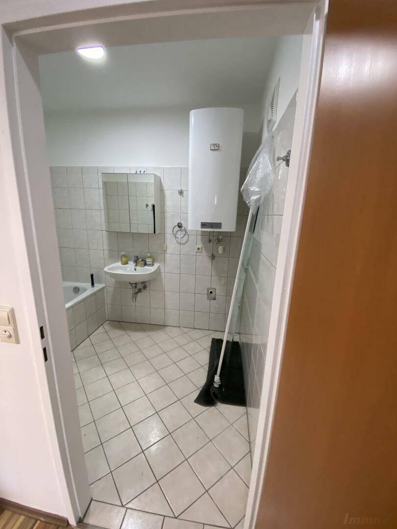 Badezimmer mit Badewanne, Waschbecken und hellen Fliesen, durch eine Tür gesehen.